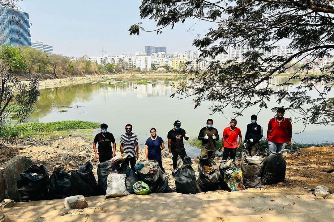 Volunteers lined up with their filled trash bags beside Lanco Hills Lake, with the city behind